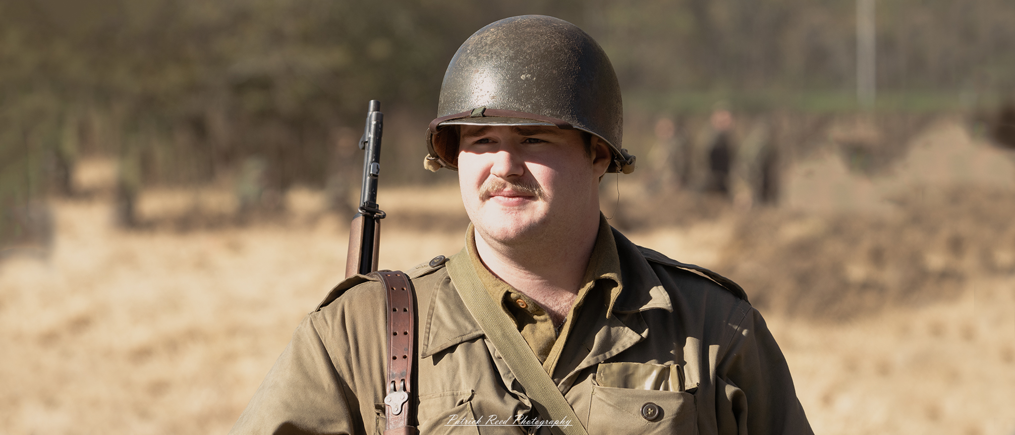 "A close-up portrait of an American soldier at the Lauer Farms WWII reenactment, fully dressed in authentic period uniform. The soldier's face shows a deep focus, embodying the grit and determination of those who served in World War II. His helmet is slightly scuffed, and the backdrop features vintage military tents and equipment, recreating the historical atmosphere of the 1940s. The setting and attire evoke the courage and resilience of U.S. troops during the war."